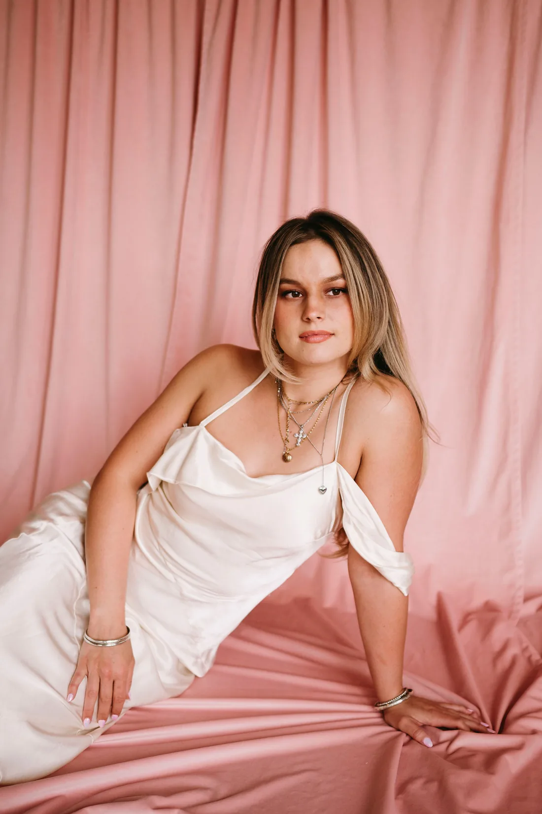 Emilee, fine-line tattoo artist, photographed against pink satin